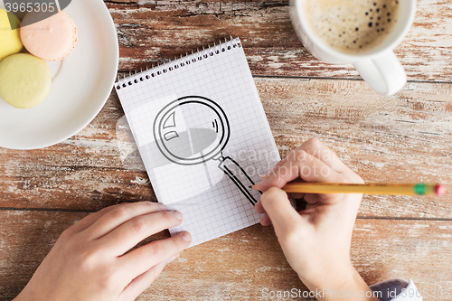 Image of close up of hands drawing magnifier in notebook