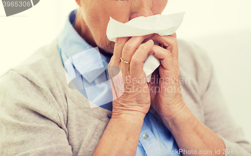 Image of sick senior woman blowing nose to paper napkin