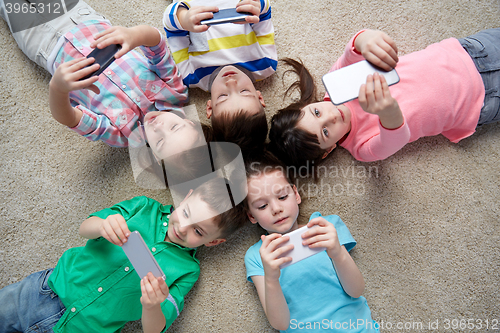Image of happy children with smartphones lying on floor