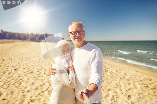 Image of seniors taking picture with selfie stick on beach