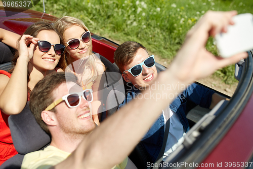 Image of friends driving in cabriolet car and taking selfie