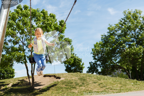 Image of happy little girl swinging on swing at playground