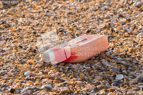 Image of Plastic bottles of engine oil on the beach is strewn with small colorful sea shells