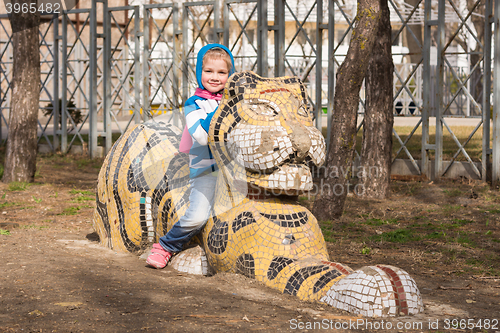 Image of Happy girl sitting on a sculpture of a tiger on the playground in Anapa