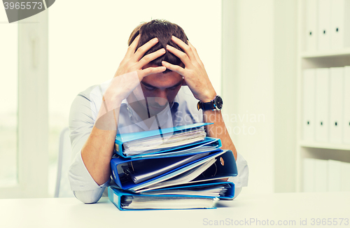 Image of sad businessman with stack of folders at office