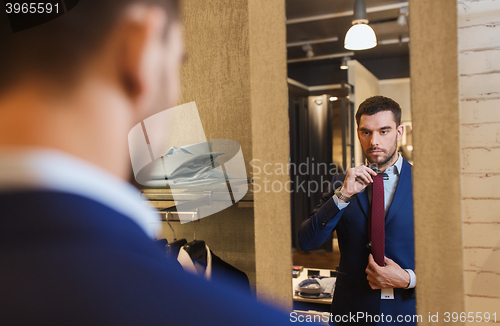 Image of man trying tie on at mirror in clothing store