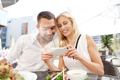 Image of happy couple with smatphone at restaurant terrace