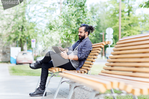 Image of man with tablet pc sitting on city street bench