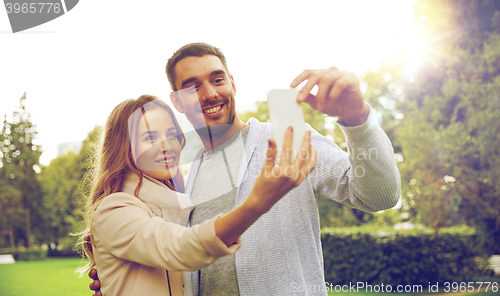 Image of happy couple with smartphone taking selfie in park