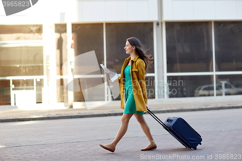 Image of happy young woman with travel bag and map in city