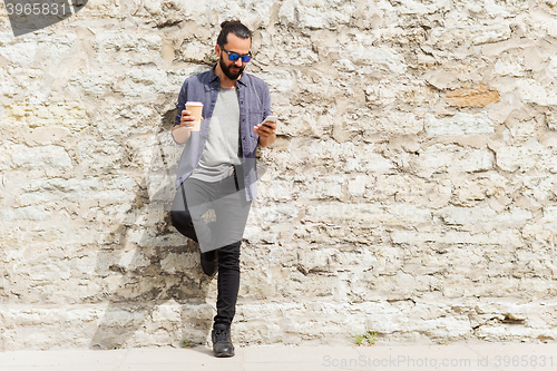 Image of man with smartphone drinking coffee on city street