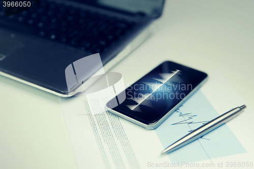 Image of close up of smartphone, laptop and pen on table