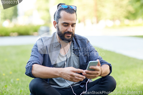 Image of man with earphones and smartphone sitting on grass