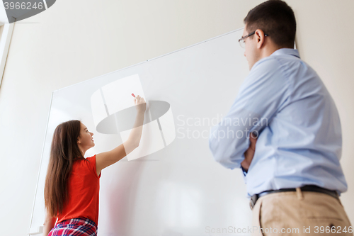 Image of student writing on board and teacher at school
