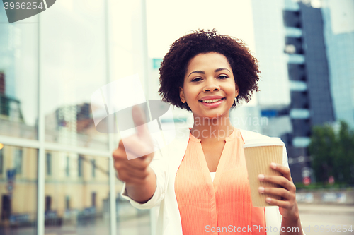 Image of happy woman with coffee showing thumbs up in city