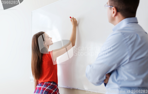 Image of student writing on board and teacher at school