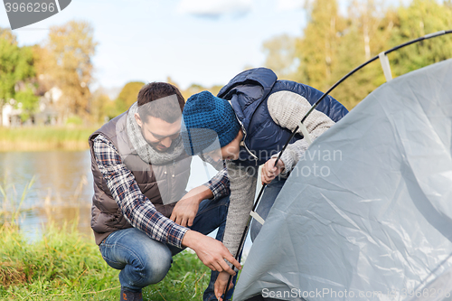 Image of happy father and son setting up tent outdoors