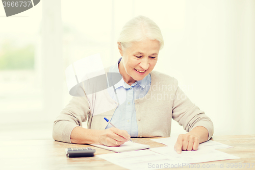 Image of senior woman with papers and calculator at home