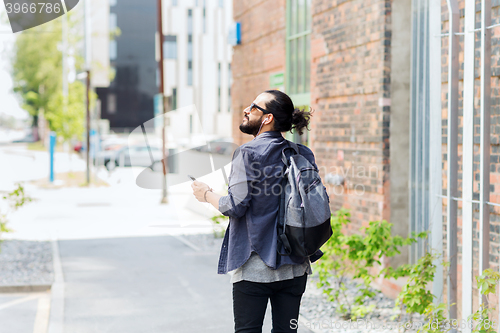 Image of man with earphones and smartphone walking in city