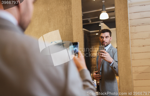 Image of man in suit taking mirror selfie at clothing store