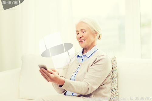 Image of senior woman with smartphone texting at home