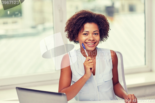 Image of happy african woman with laptop at office