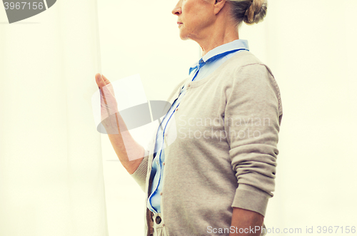 Image of lonely senior woman looking through window at home