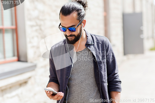 Image of man with earphones and smartphone walking in city