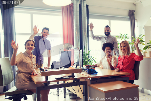 Image of happy creative team waving hands in office