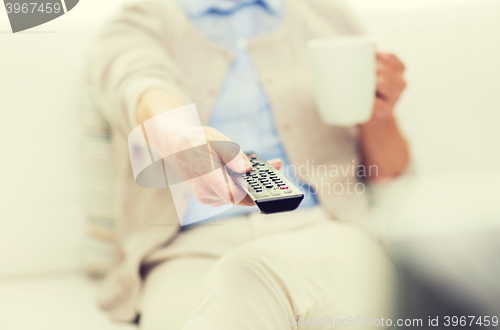 Image of senior woman watching tv and drinking tea at home