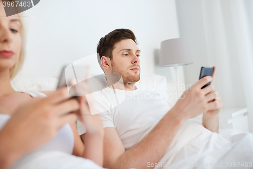 Image of couple with smartphones in bed