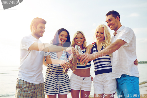 Image of smiling friends clinking bottles on beach