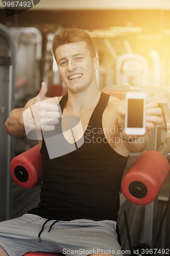 Image of smiling young man with smartphone in gym