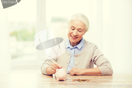 Image of senior woman putting money to piggy bank at home