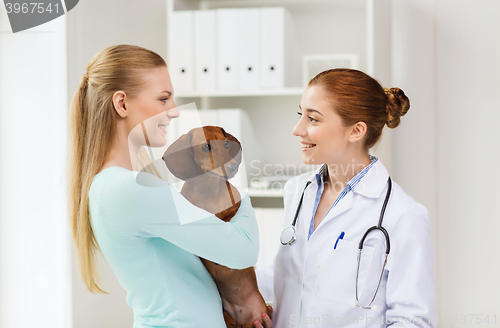 Image of happy woman with dog and doctor at vet clinic