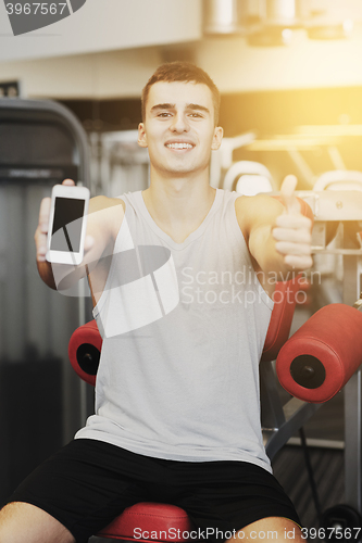 Image of smiling young man with smartphone in gym