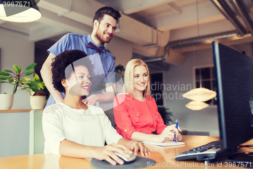 Image of happy creative team with computer in office