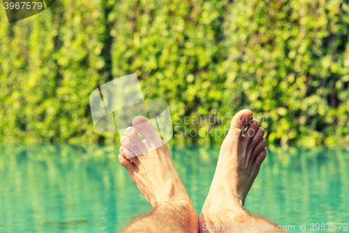 Image of close up of male feet over resort swimming pool