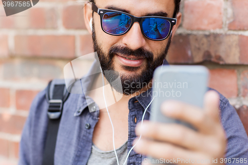 Image of man with earphones and smartphone on city street