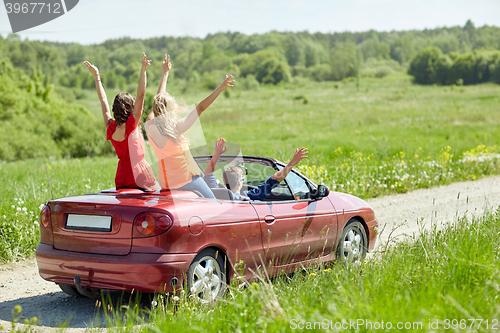 Image of happy friends driving in cabriolet car at country