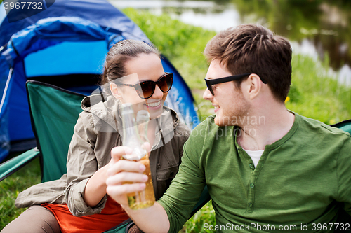 Image of happy couple clinking drinks at campsite tent