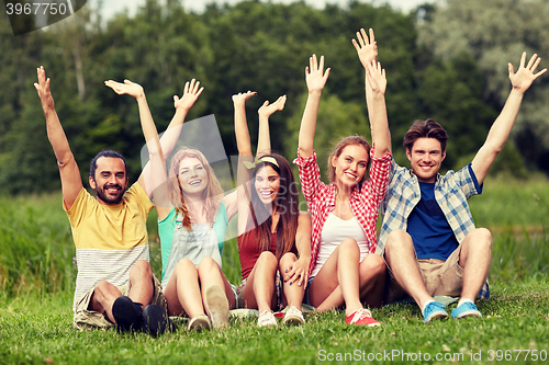 Image of group of smiling friends waving hands outdoors