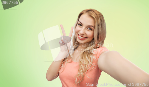 Image of smiling woman taking selfie and showing peace sign