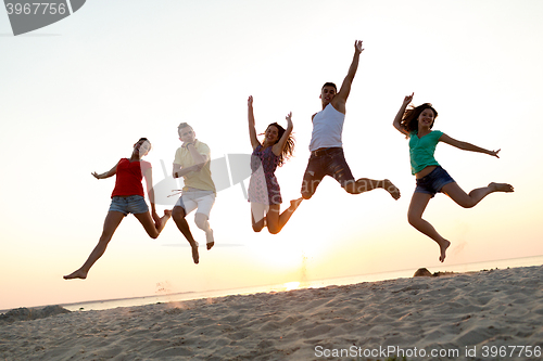 Image of smiling friends dancing and jumping on beach