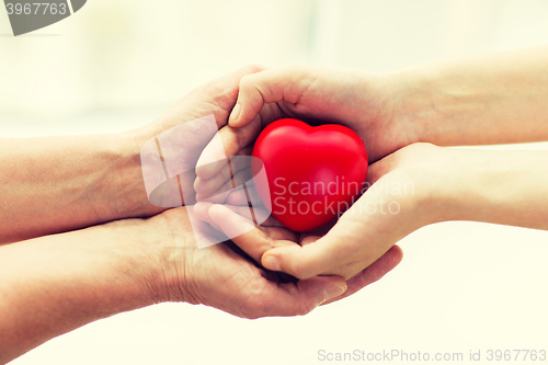 Image of senior and young woman hands holding red heart