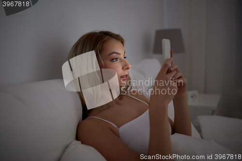 Image of young woman with smartphone in bed at home bedroom