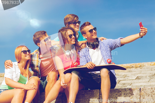 Image of group of smiling friends with smartphone outdoors