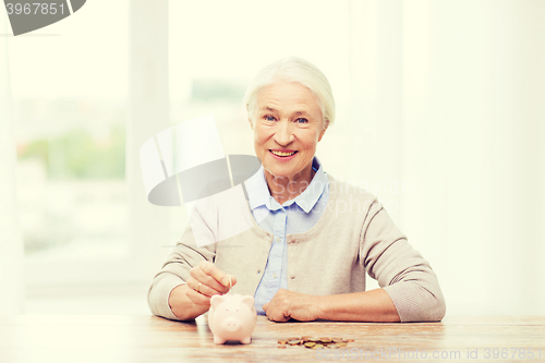 Image of senior woman putting money to piggy bank at home