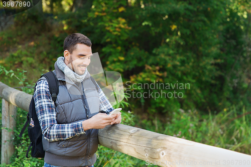 Image of happy man with backpack and smartphone outdoors