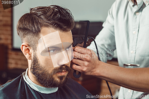 Image of The hands of young barber making haircut to attractive man in barbershop